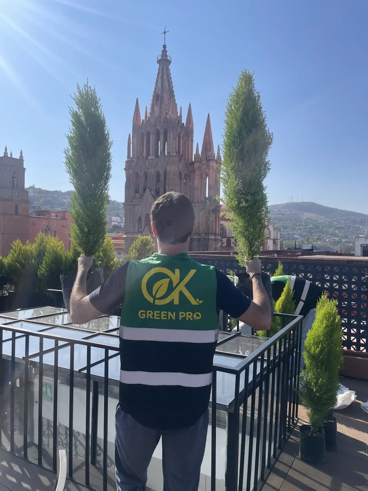 Integrante del equipo Green Pro con uniforme sosteniendo dos cipreses